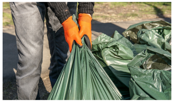 A person wearing gloves is picking up a garbage bag from the curb.