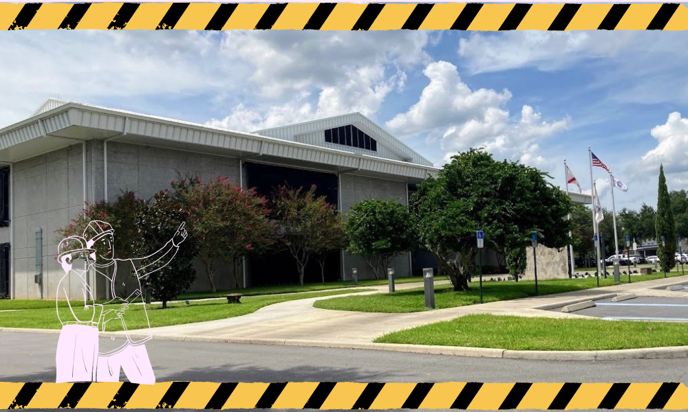 This is a side view of the Emergency Operations Center, which is surrounded by small trees and has three large flag poles. In the picture, there are two cartoon construction workers standing in front of the building and pointing upwards, while construction tape frames the top and bottom of the image.