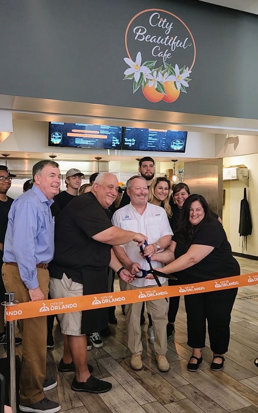 Owner of City Beautiful Cafe commemorates the grand opening with a ribbon cutting ceremony. He is joined by city officials and staff members.