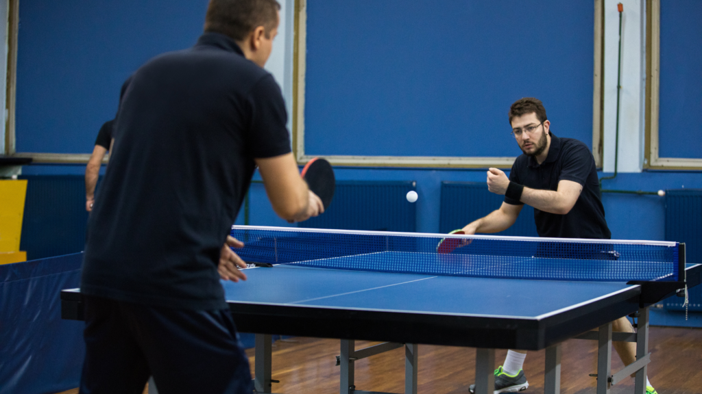 Two people playing ping pong in a gymnasium