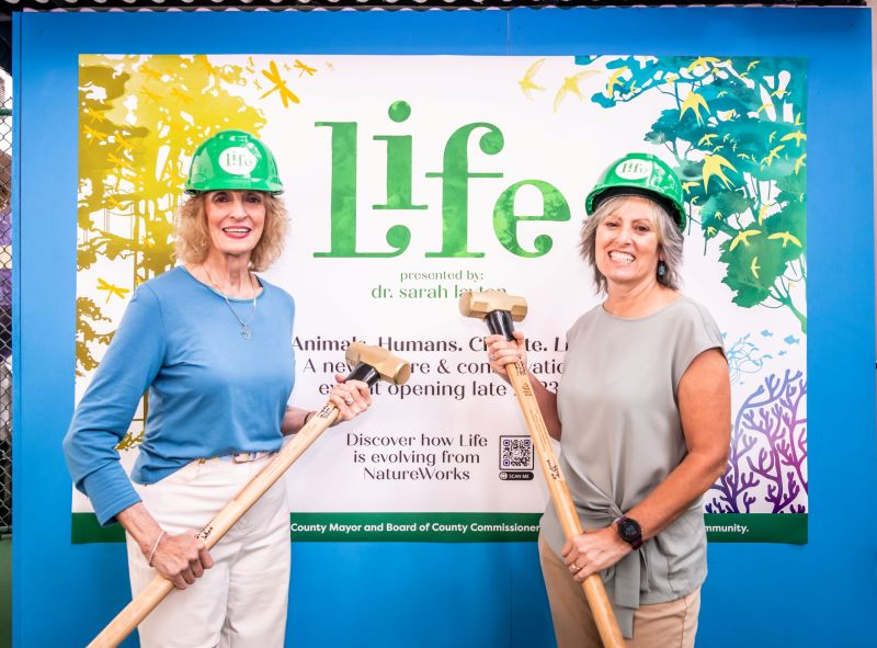 Dr. Sarah Layton and JoAnn Newman in front of the OSC Life Exhibit signage with sledge hammers