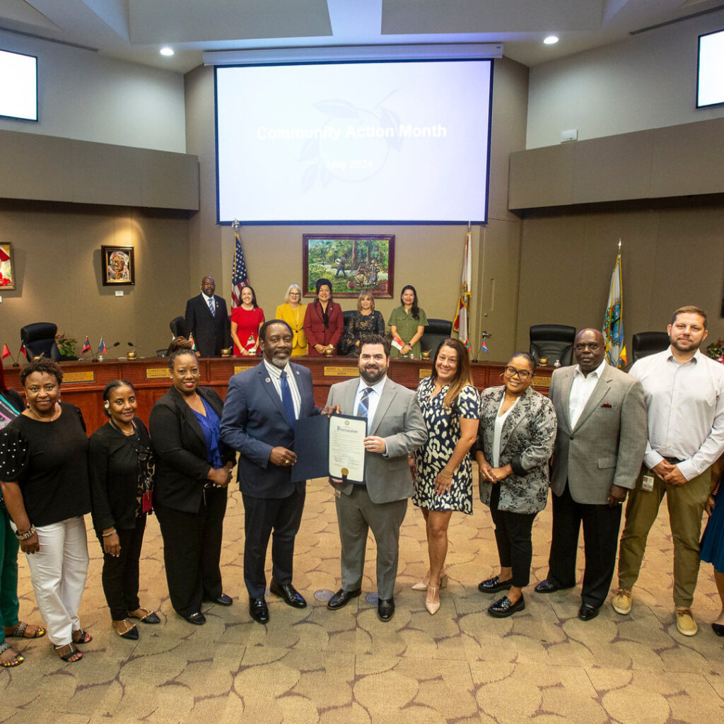 This is a photograph of Orange County Mayor Jerry Demings and the Community Action Division being presented with their Proclamation. In the background are the County Commissioners in attendance