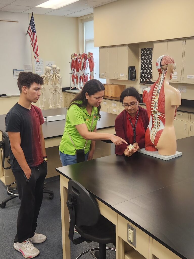 photograph of Emily Bonilla, her son, and a Valencia professor examining parts of the spine on an anatomy dummy